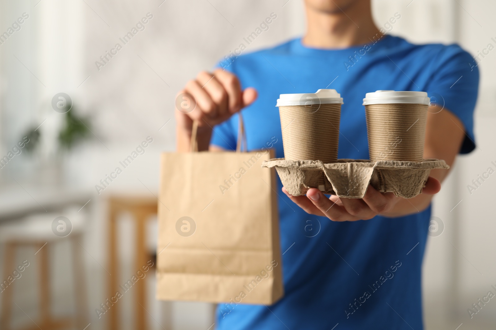 Photo of Fast-food worker with paper bag and cups indoors, closeup