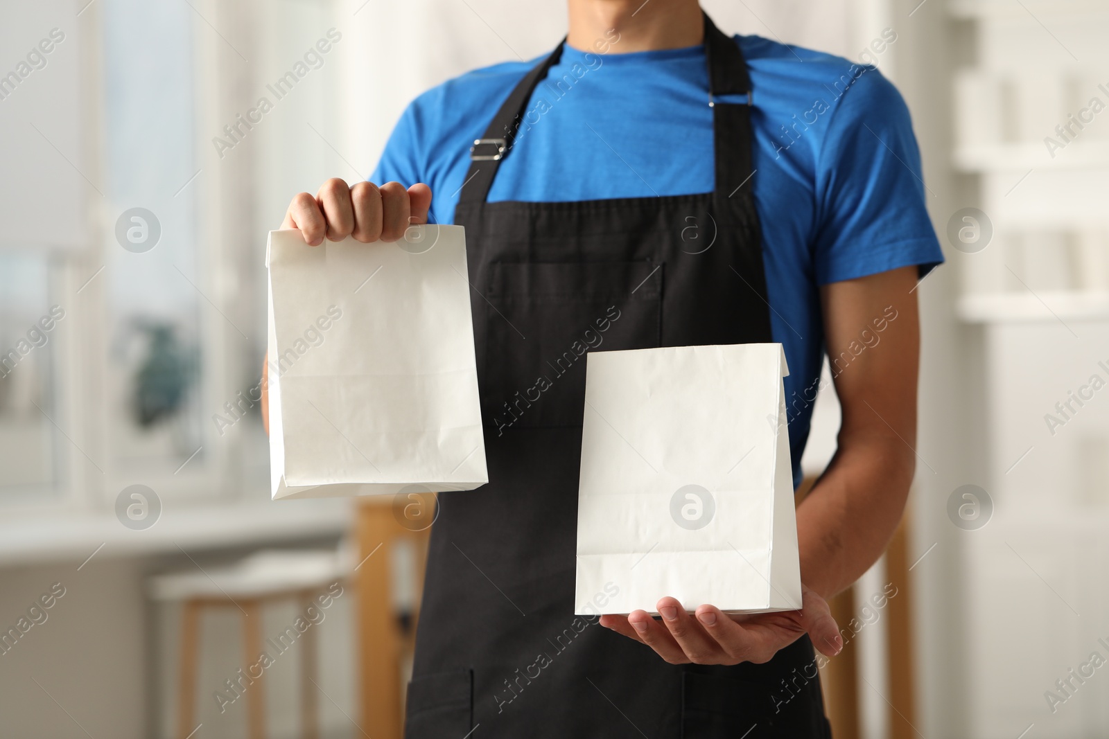 Photo of Fast-food worker with paper bags indoors, closeup