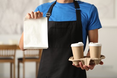 Photo of Fast-food worker with paper bag and cups indoors, closeup