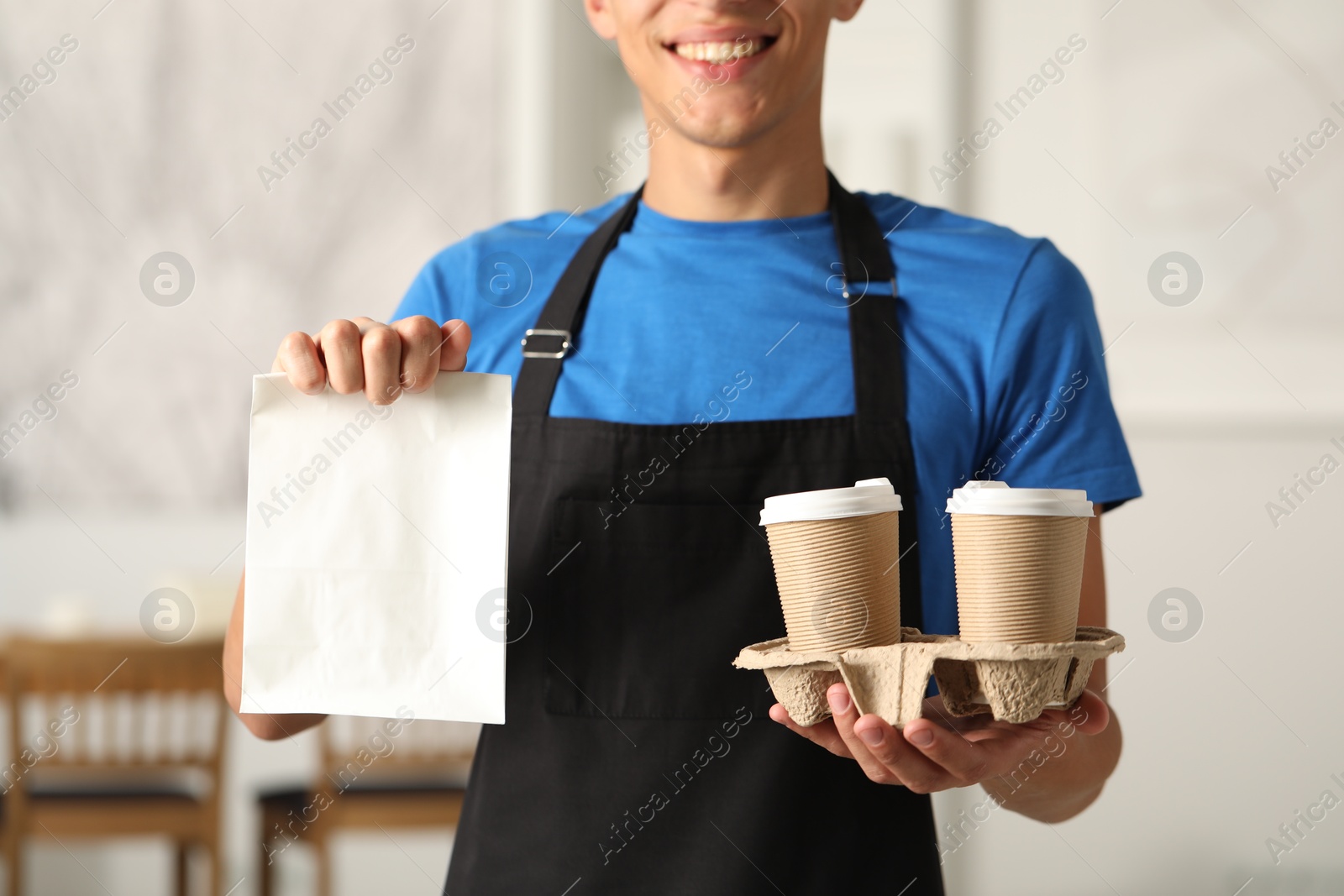 Photo of Fast-food worker with paper bag and cups indoors, closeup