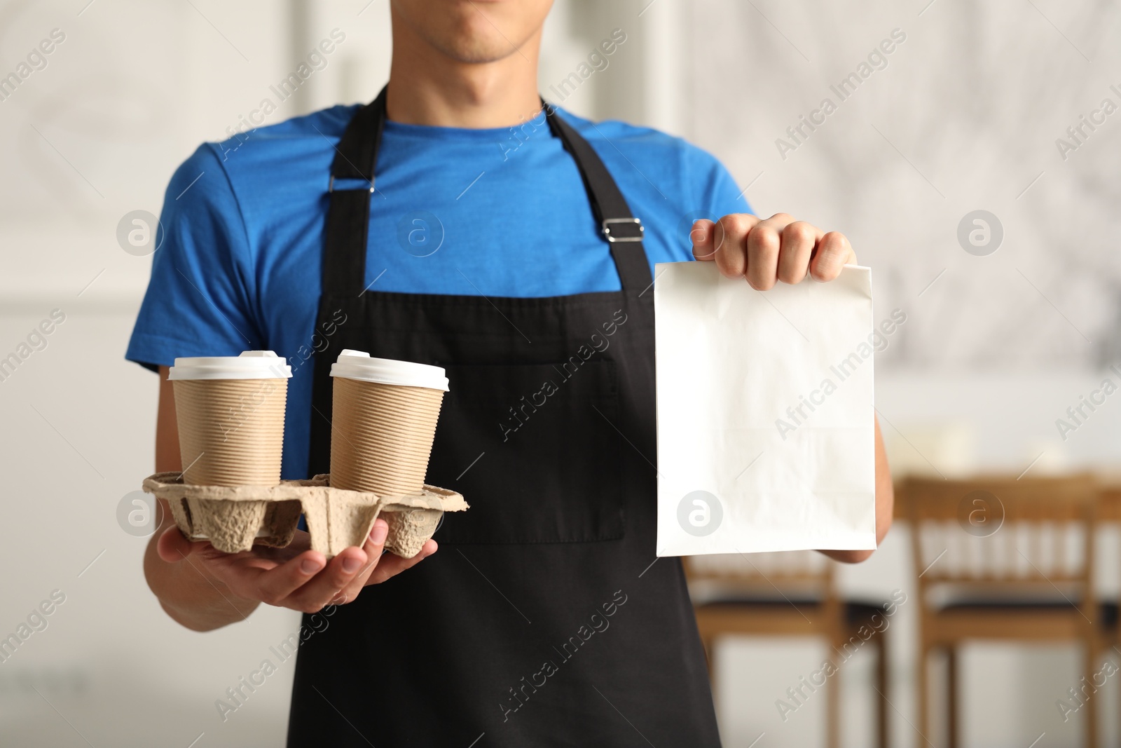 Photo of Fast-food worker with paper bag and cups indoors, closeup