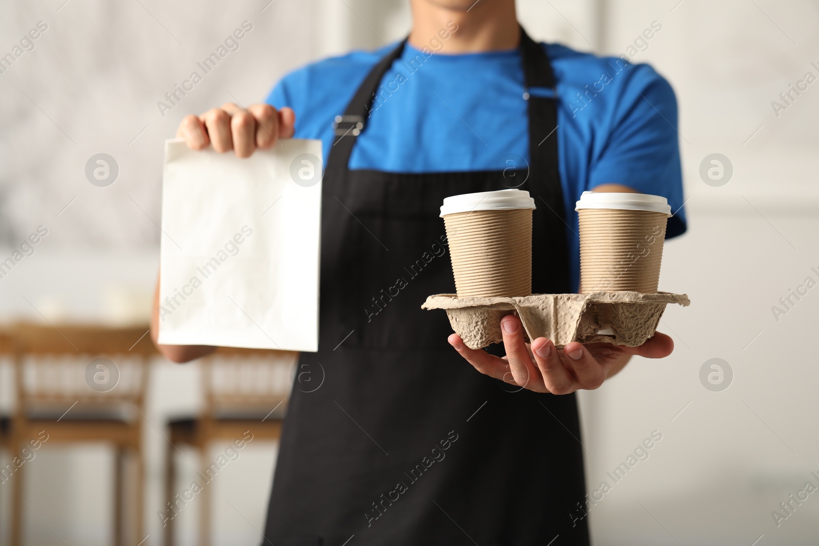 Photo of Fast-food worker with paper bag and cups indoors, closeup