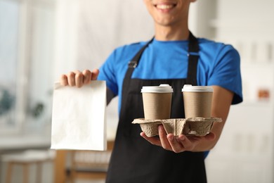 Photo of Fast-food worker with paper bag and cups indoors, closeup