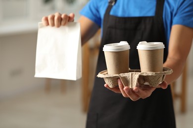 Photo of Fast-food worker with paper bag and cups indoors, closeup