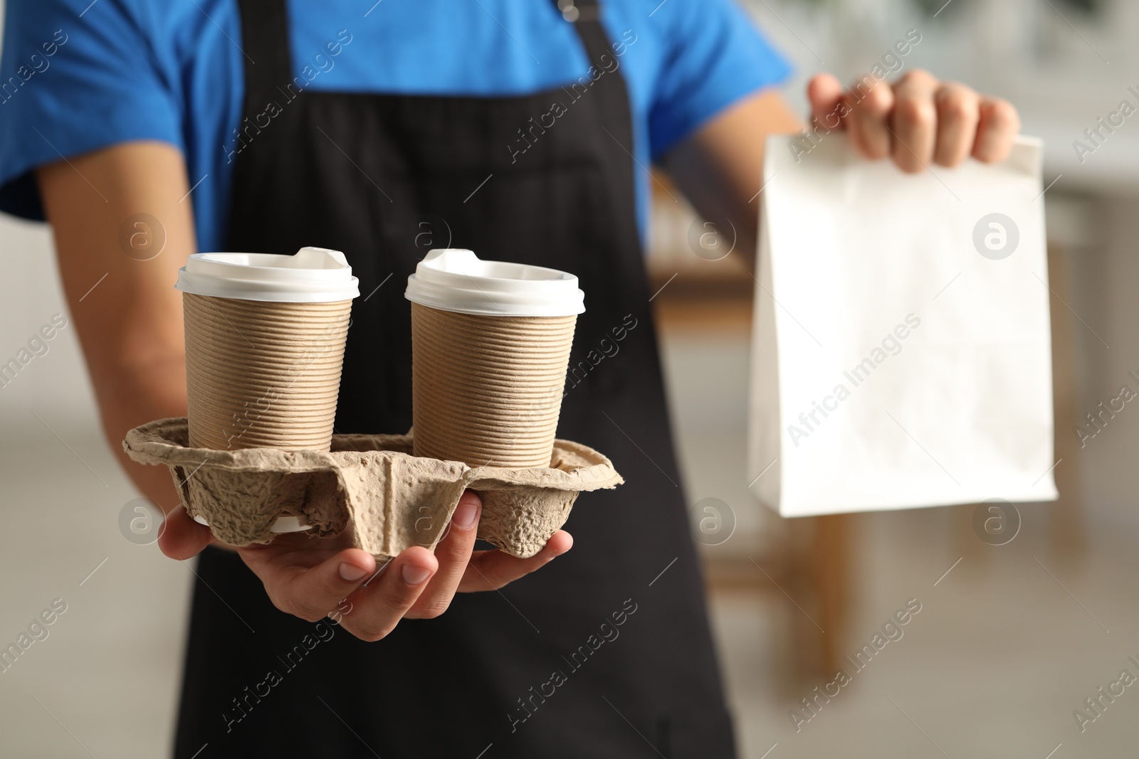 Photo of Fast-food worker with paper bag and cups indoors, closeup