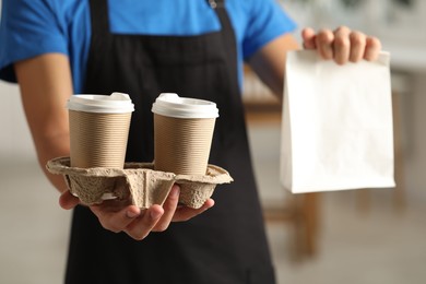 Fast-food worker with paper bag and cups indoors, closeup