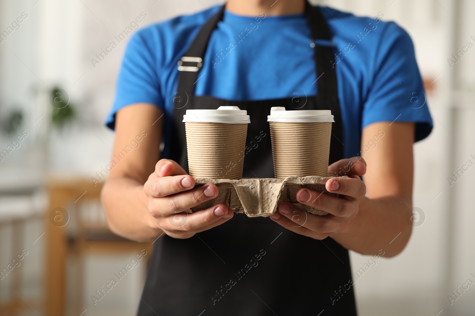 Photo of Fast-food worker with paper cups indoors, closeup