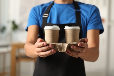 Photo of Fast-food worker with paper cups indoors, closeup