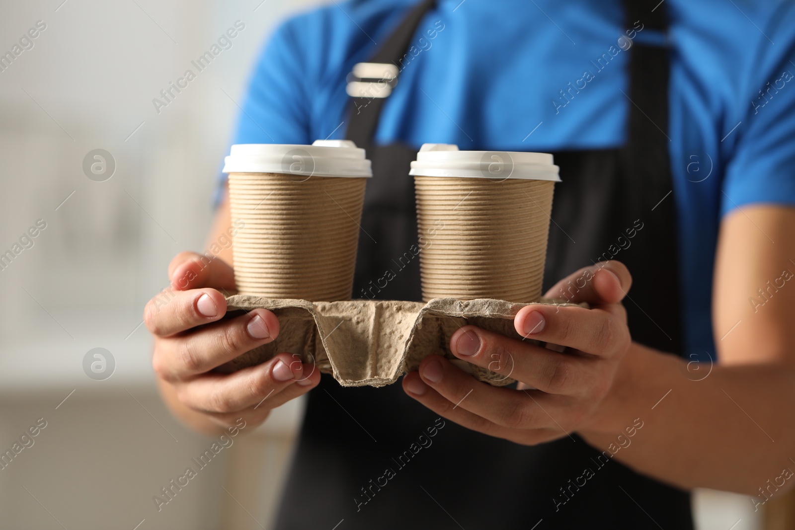 Photo of Fast-food worker with paper cups indoors, closeup