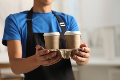 Photo of Fast-food worker with paper cups indoors, closeup