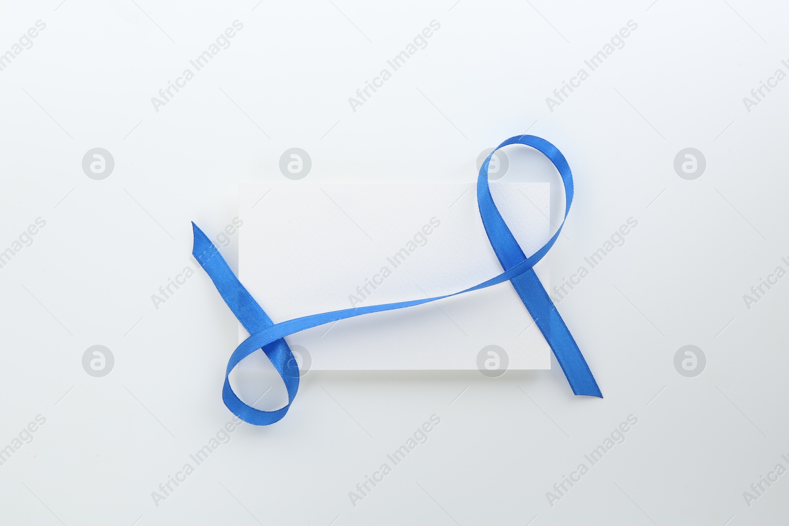 Photo of Blank card and blue ribbon on white background, top view