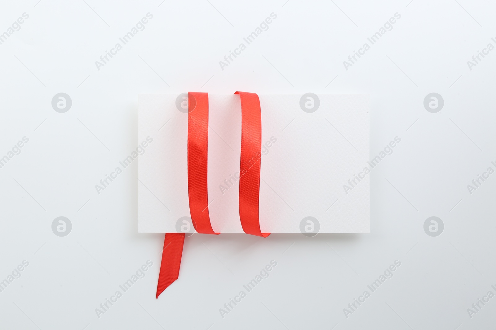 Photo of Blank card and red ribbon on white background, top view