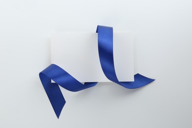 Photo of Blank card and blue ribbon on white background, top view