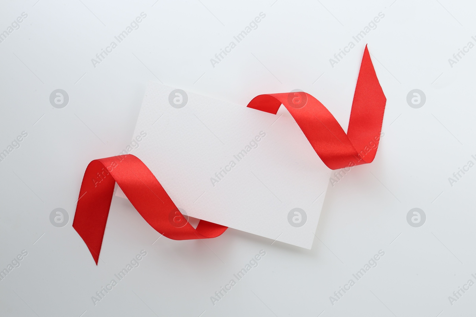 Photo of Blank card and red ribbon on white background, top view