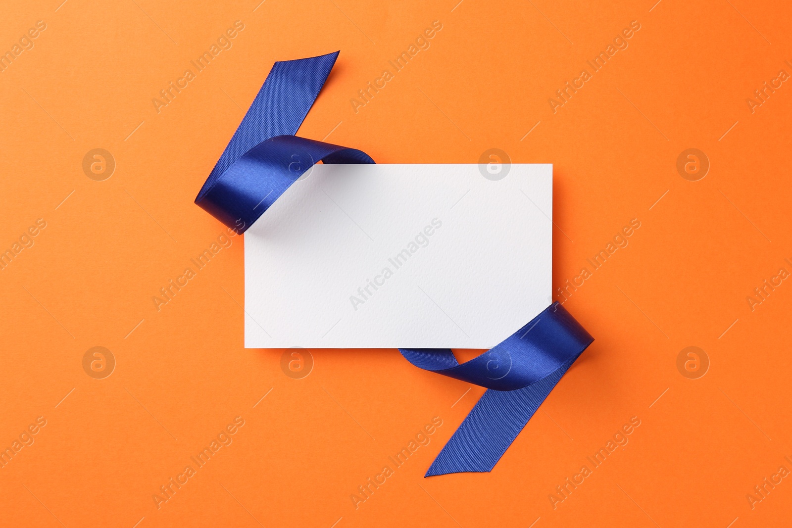 Photo of Blank card and blue ribbon on orange background, top view