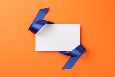 Photo of Blank card and blue ribbon on orange background, top view