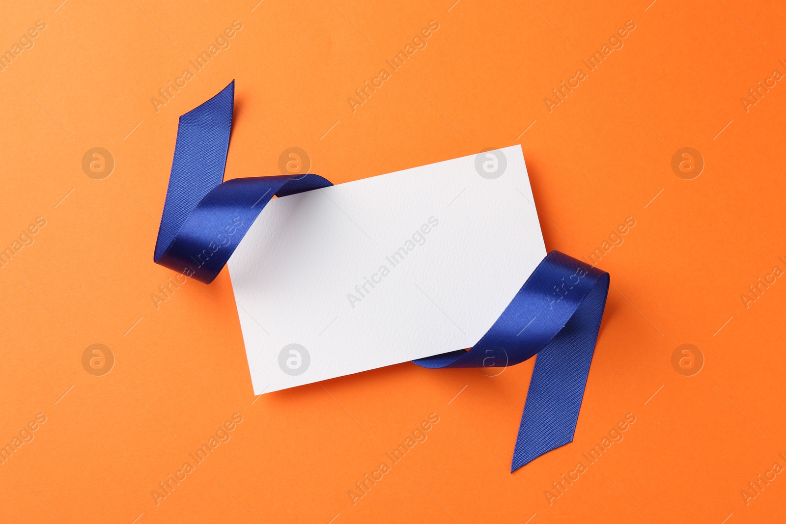 Photo of Blank card and blue ribbon on orange background, top view