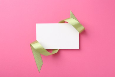 Photo of Blank card and olive ribbon on pink background, top view