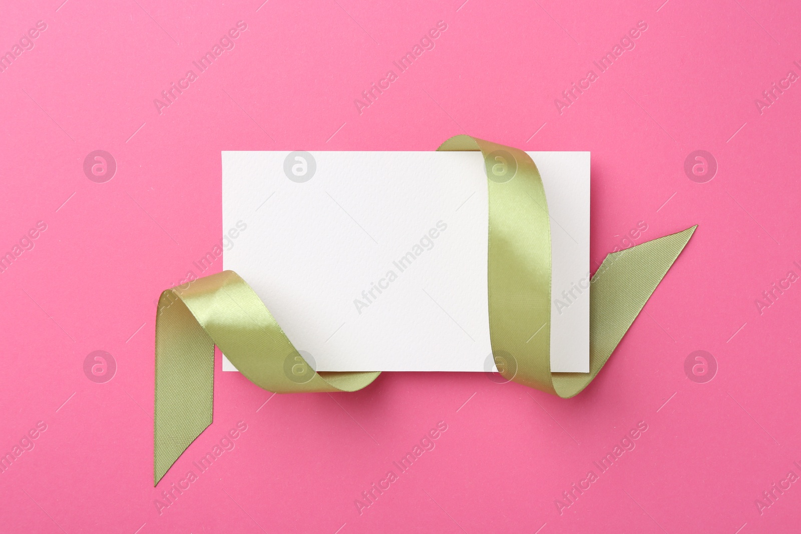 Photo of Blank card and olive ribbon on pink background, top view