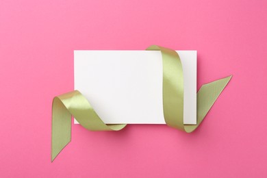 Photo of Blank card and olive ribbon on pink background, top view