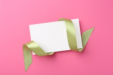 Blank card and olive ribbon on pink background, top view