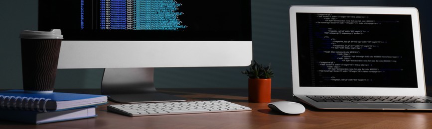 Programmer's workplace. Modern computer with unfinished code, laptop and other supplies on wooden desk. Banner design