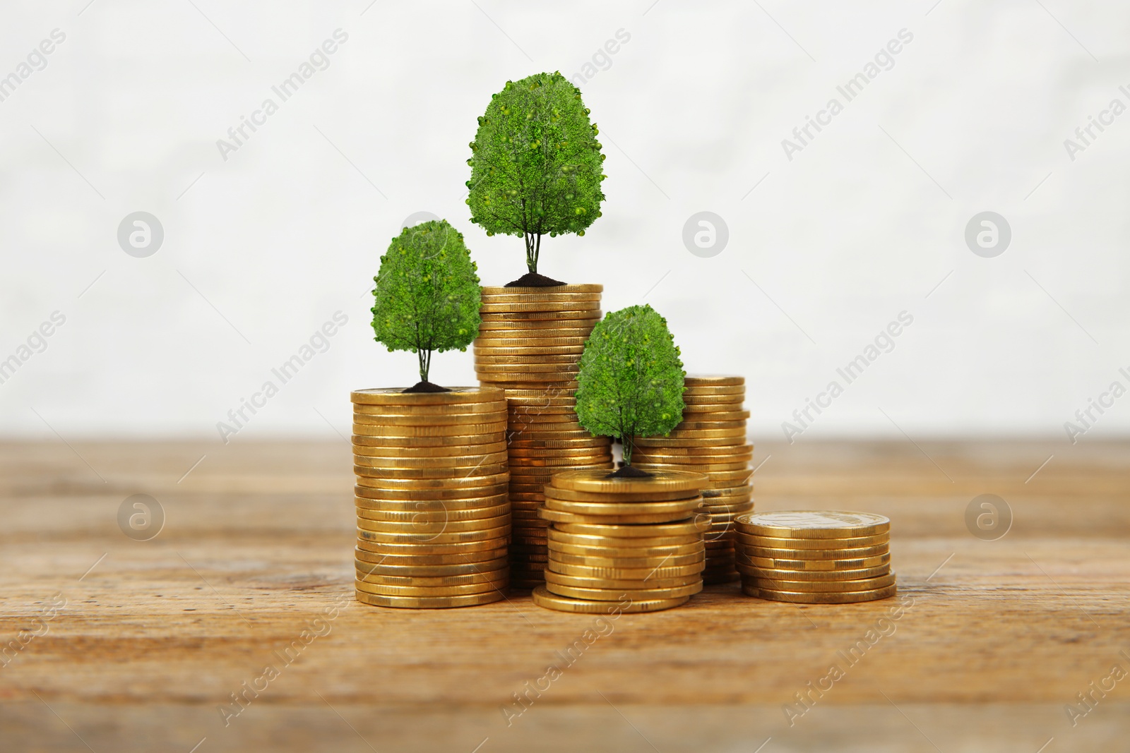 Image of Stacked coins with tiny green trees on wooden table