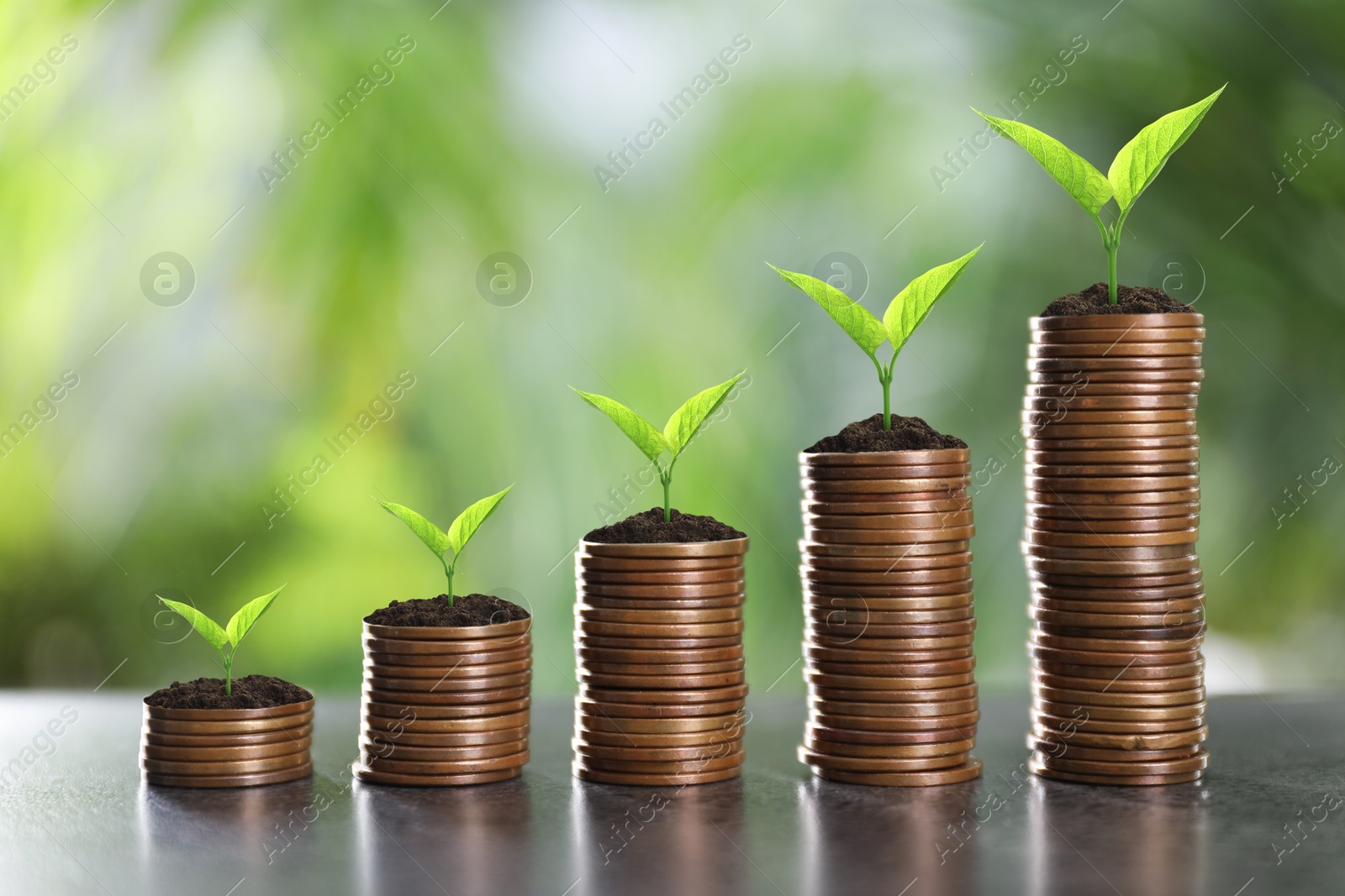 Image of Stacked coins with green seedlings on table against blurred background