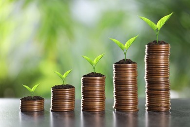 Image of Stacked coins with green seedlings on table against blurred background