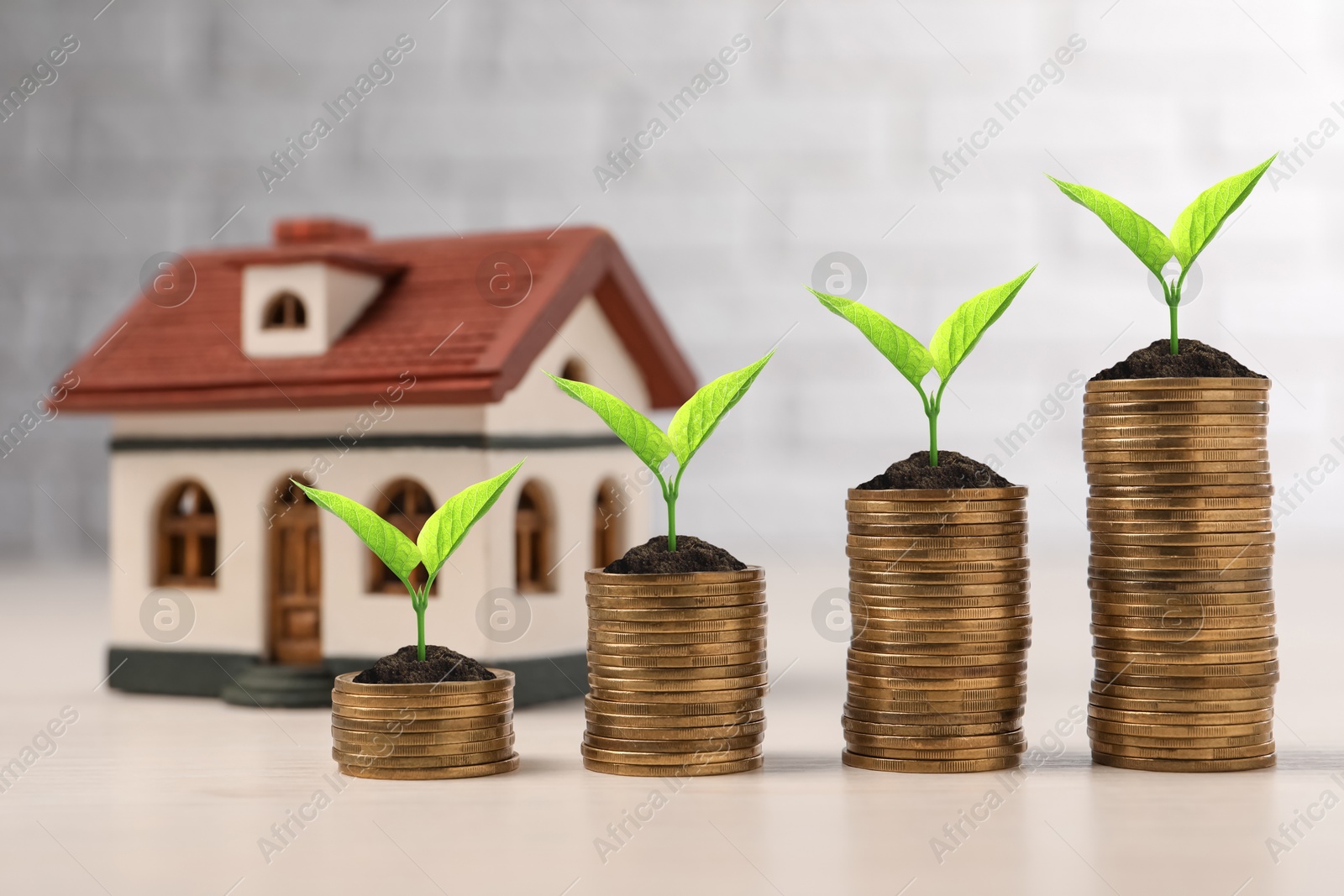 Image of Stacked coins with green seedlings and house model on table