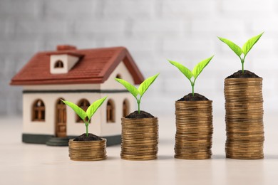 Image of Stacked coins with green seedlings and house model on table