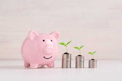 Image of Stacked coins with green seedlings and piggy bank on white table