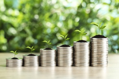 Image of Stacked coins with green seedlings on table against blurred background