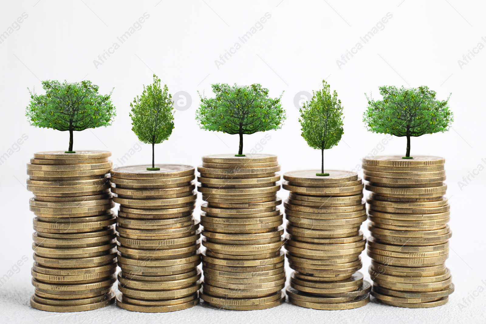 Image of Stacked coins with tiny green trees on white background