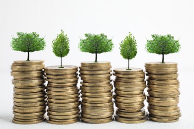 Image of Stacked coins with tiny green trees on white background