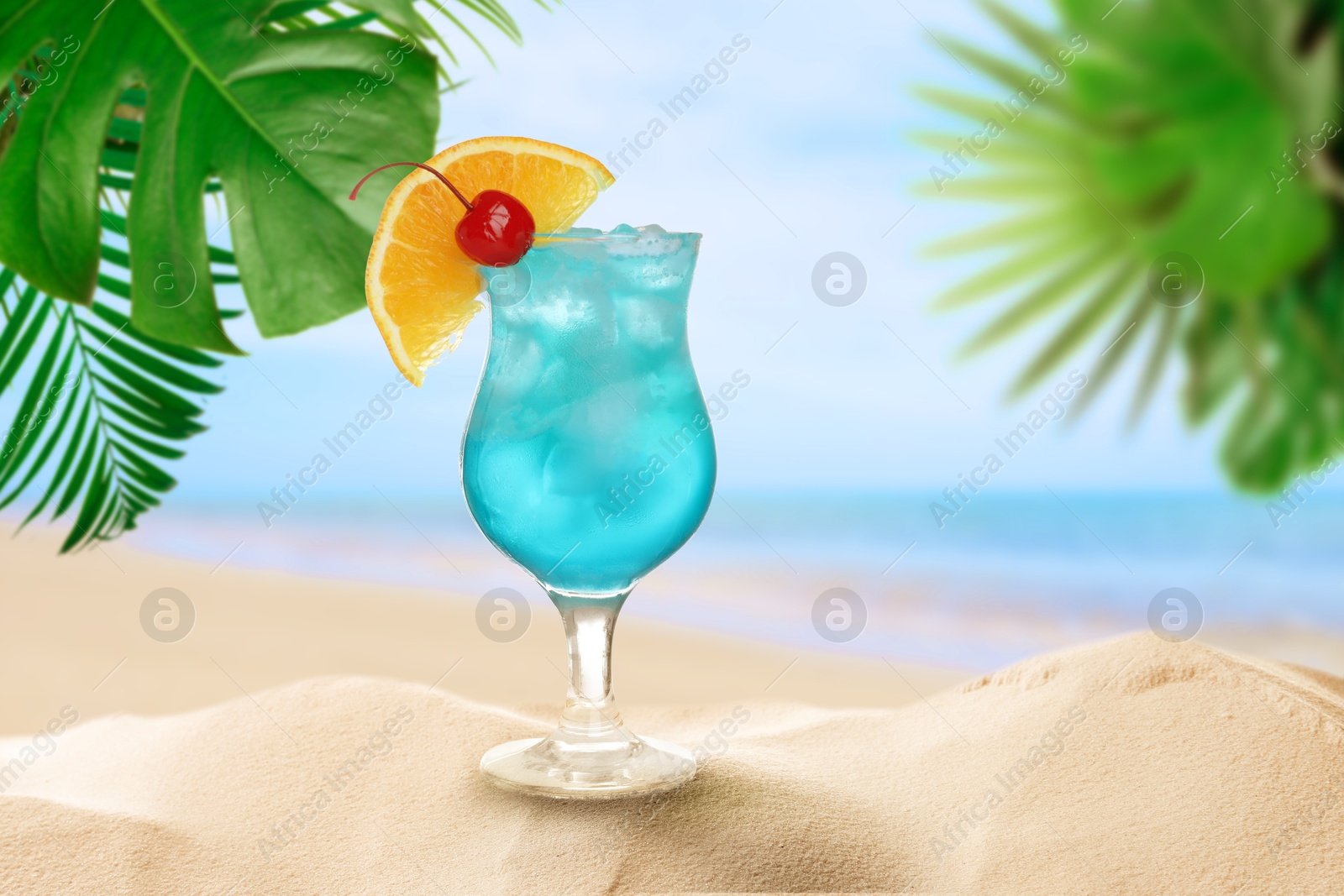 Image of Summer beach with delicious Blue Lagoon cocktail, tropical leaves and golden sand