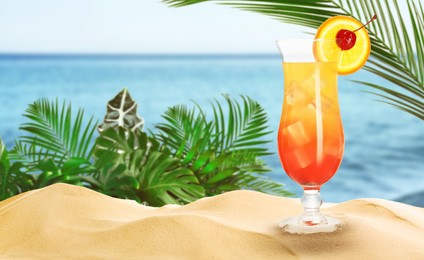 Image of Summer beach with delicious Tequila Sunrise cocktail, tropical leaves and golden sand, space for text