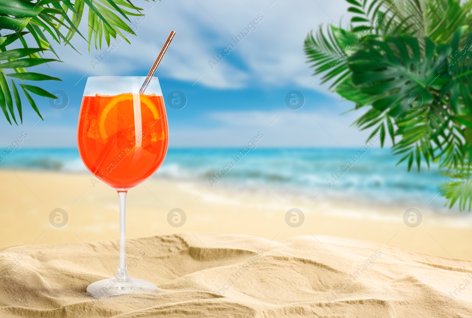 Image of Summer beach with Aperol Spritz delicious cocktail, tropical leaves and golden sand