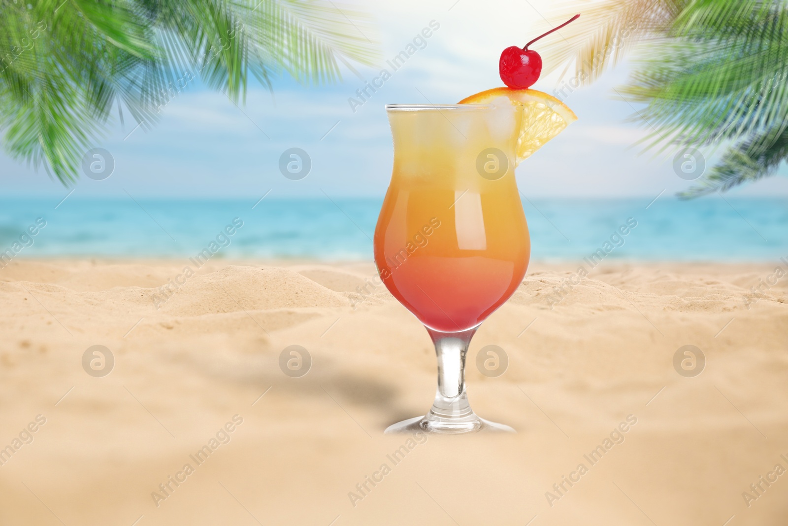 Image of Summer beach with delicious Tequila Sunrise cocktail, palm leaves and golden sand