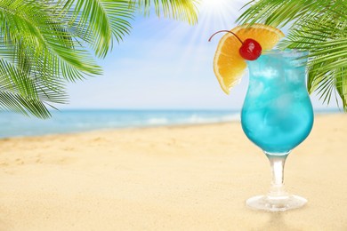 Image of Summer beach with delicious Blue Lagoon cocktail, palm leaves and golden sand, space for text