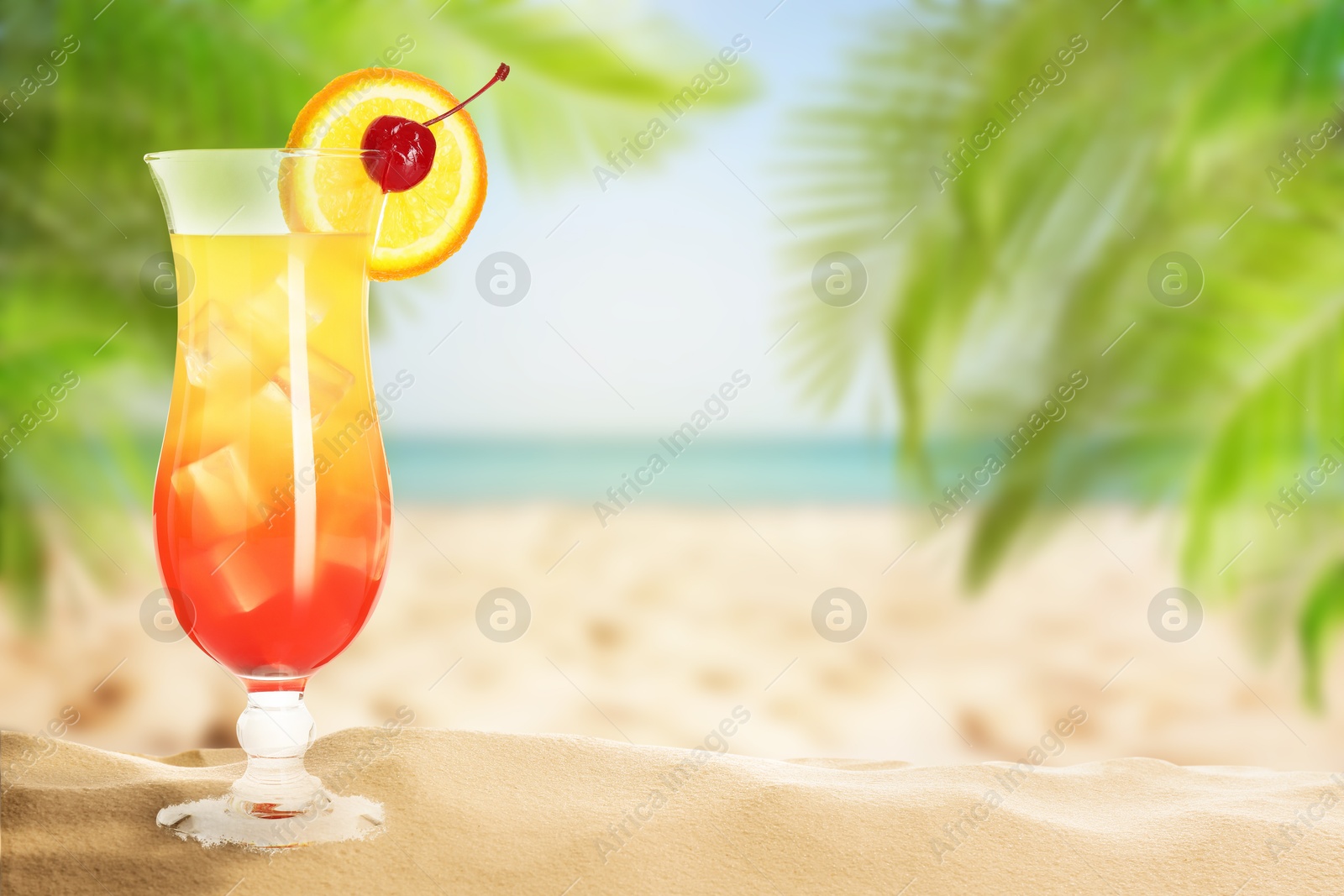 Image of Summer beach with delicious Tequila Sunrise cocktail, palm leaves and golden sand, space for text