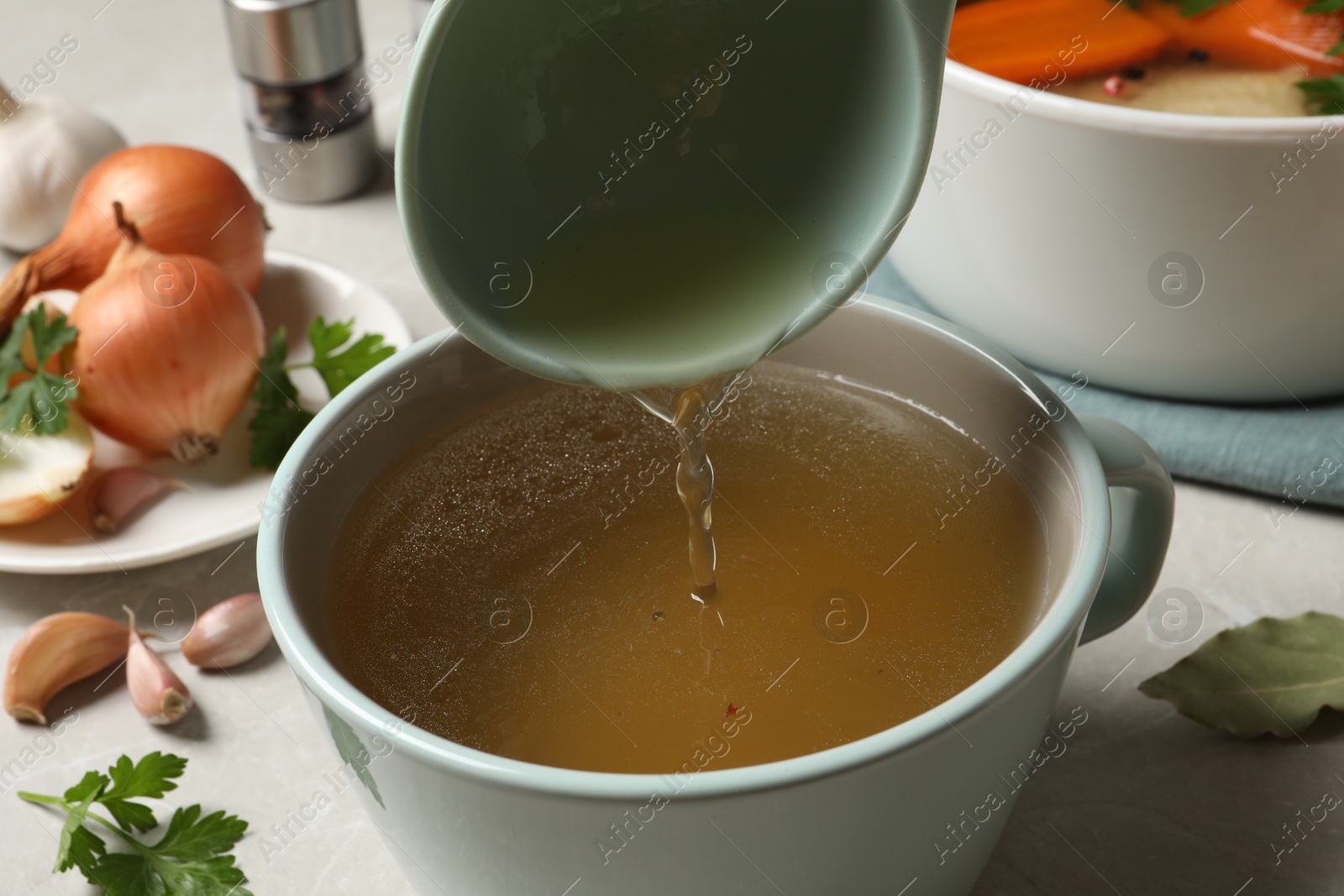 Photo of Pouring hot delicious bouillon into cup on light grey table, closeup