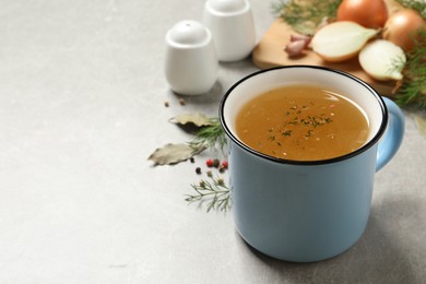 Photo of Hot delicious bouillon with dill in cup on light grey table. Space for text