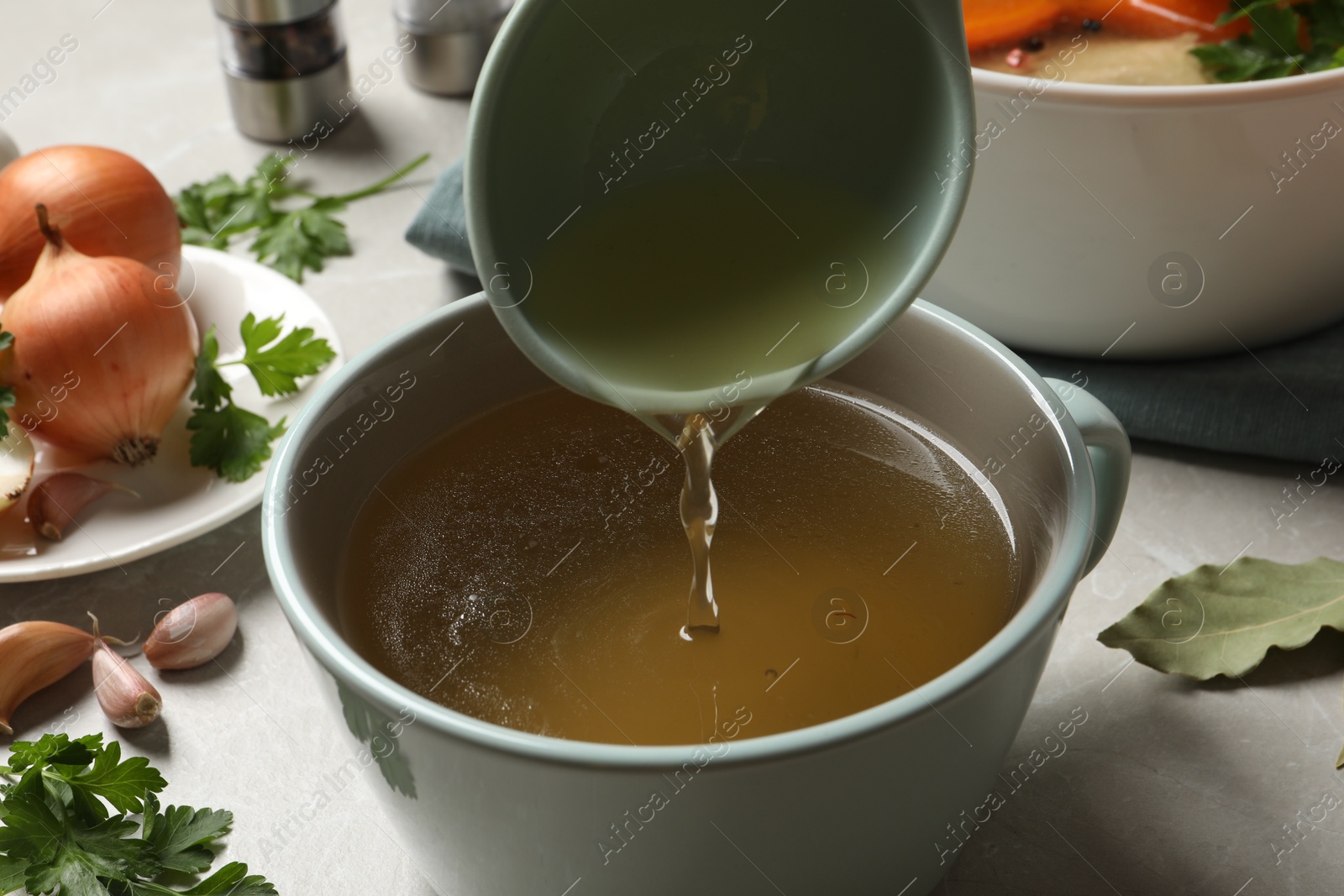 Photo of Pouring hot delicious bouillon into cup on light grey table, closeup