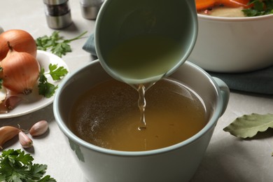 Pouring hot delicious bouillon into cup on light grey table, closeup