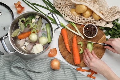 Photo of Cooking tasty bouillon. Woman cutting celery at white table, top view