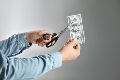 Photo of Budgeting. Man cutting dollar banknote with scissors on light grey background, closeup