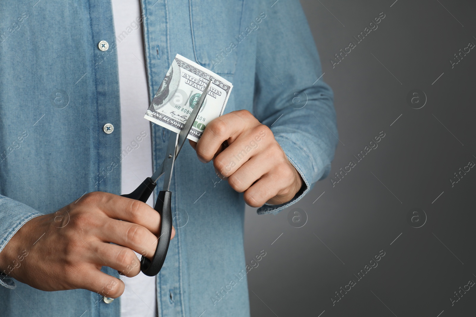 Photo of Budgeting. Man cutting dollar banknote with scissors on dark grey background, closeup. Space for text