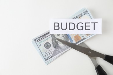 Photo of Dollar banknotes, scissors and paper with word Budget on white background, top view. Space for text