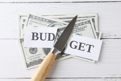 Cut paper with word Budget, dollar banknotes and knife on white wooden table, top view